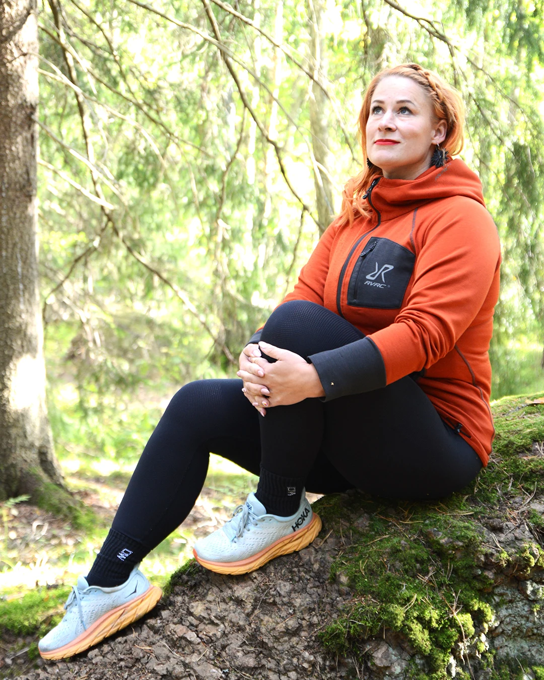 Saara istuu metsässä sammaleisella kalliolla.